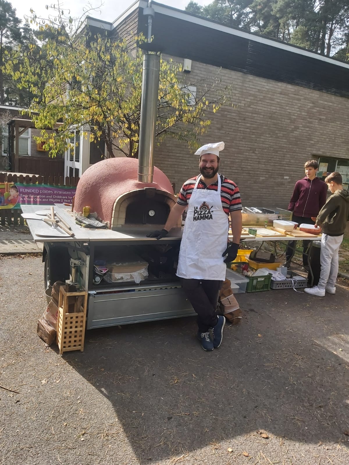 Pizza chef posing beside mobile wood-fired pizza oven at outdoor event