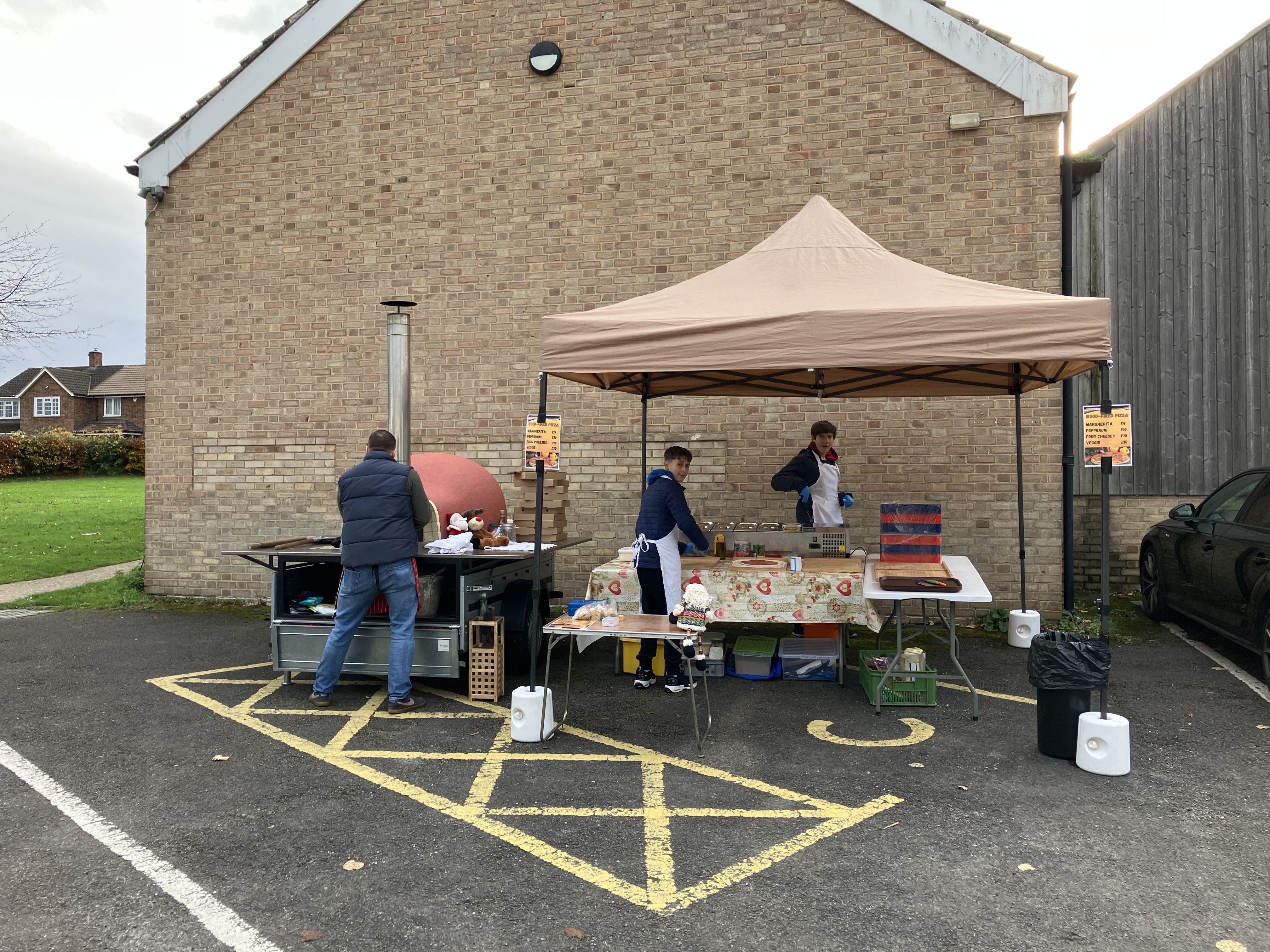 Mobile pizza stand with wood-fired oven set up under tent in parking lot